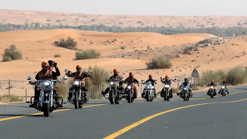 A group of riders crossing a desert road lined with dunes in the UAE